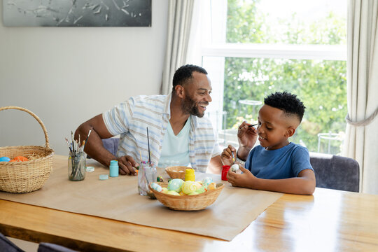 African American father and boy painting eggs at dining table with wicker baskets