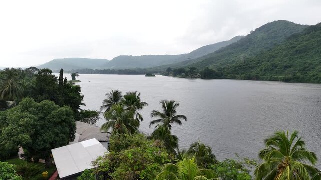Drone shot capturing the Akosombo Dam and the lush tropical surroundings of the Volta River in Ghana. High-angle view of West African infrastructure and nature scenery.