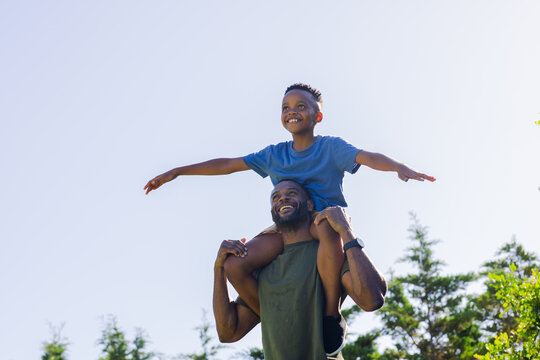 African American father carrying son in park, wearing green tank and watch, child wearing blue tee