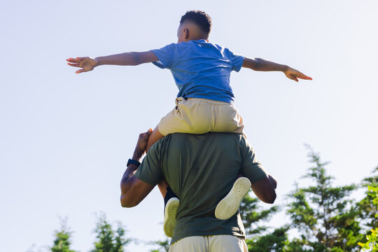 African American mature man carrying boy on shoulders, steadying legs in park, white sneakers