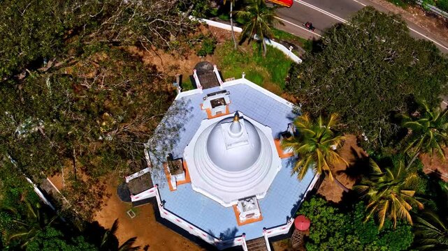 An overhead drone shot captures a white octagonal stupa or pagoda surrounded by palm trees and footpaths at Nilwala Crocodile Safari, Matara.