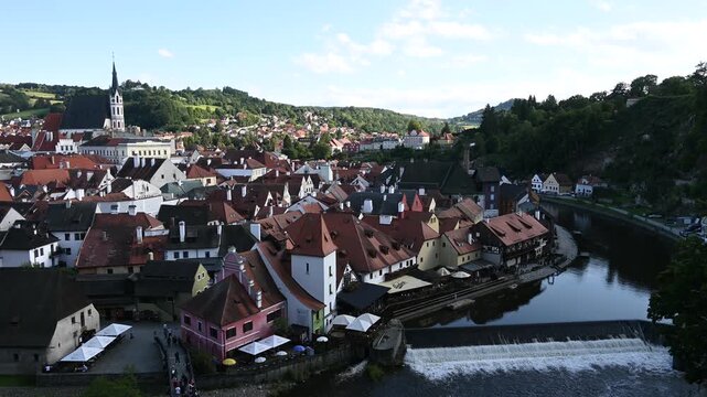 High-angle panoramic view of Cesky Krumlov during sunset. The footage captures the historic castle, the iconic round tower, and the red-roofed medieval houses nestled along the Vltava river.