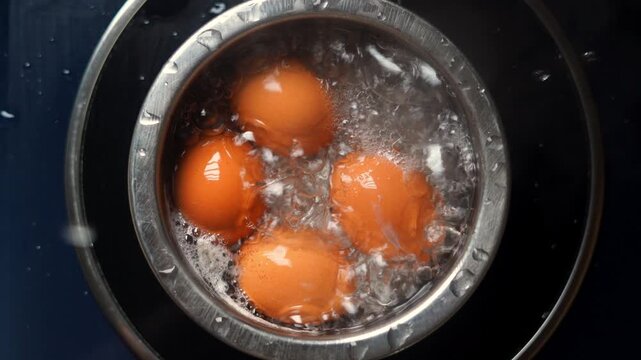 Close-up of chicken eggs boiling in stainless pan with hot water and bubbles on induction cooker. Brown shell egg boil top view