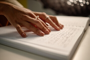 Woman hands reading braille book in library, fingers gently moving across raised dots on page, demonstrating tactile literacy and accessibility for visually impaired