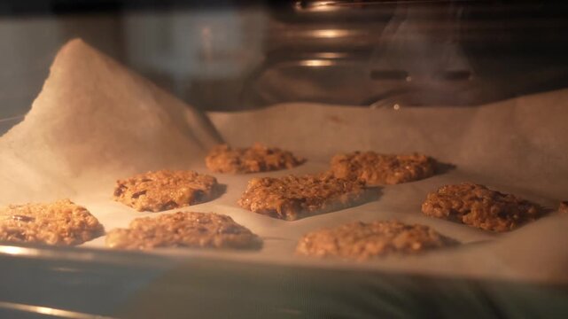 A tray of cookies is baking in an oven. The cookies are on a sheet of parchment paper