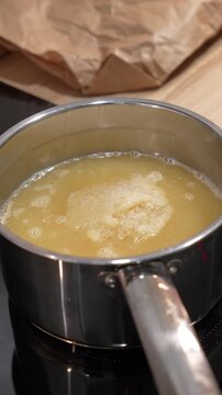 A pot of yellow liquid sits on a stove. The liquid is bubbling and he is thick