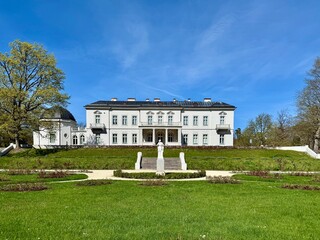 Fototapeta premium Palanga Amber Museum, located in the Palanga Botanical Garden, Lithuania, is housed in a grand white Neoclassical building with a dark roof. A statue stands prominently on a pathway 
