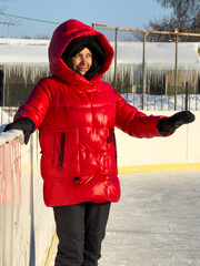A woman in a red coat is standing on a skating rink