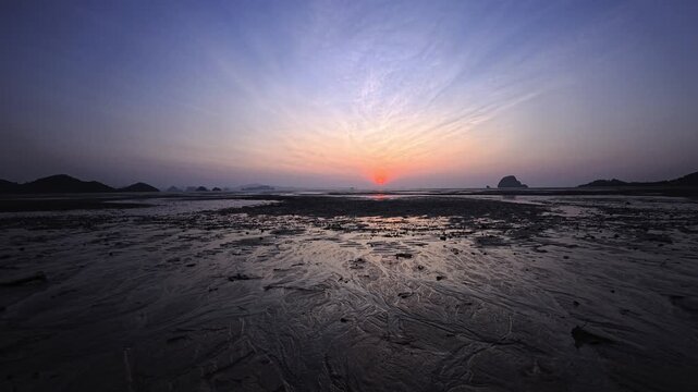 Centered sunrise over textured sand flats and distant islands in Thailand