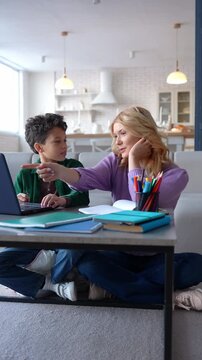 Positive cute African American schoolboy and caring attractive teenage nanny studying lesson online using laptop pc, discussing educational material at home.