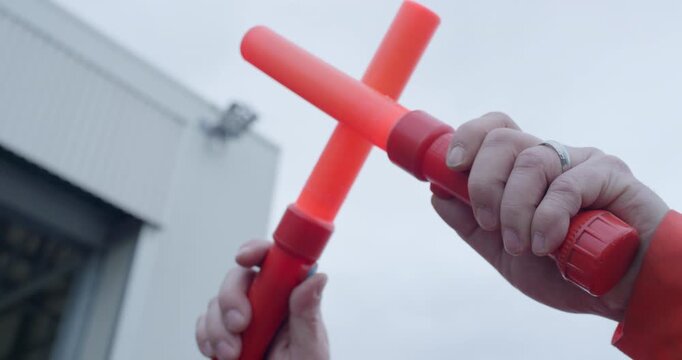 Close up of hands holding two orange illuminated aviation signal wands