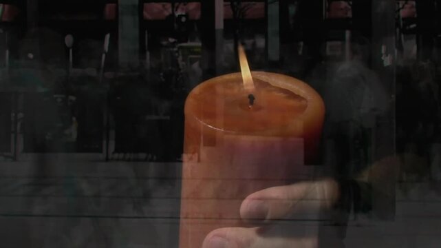 Wick lighting, flame flickering as handheld pillar candle shifting while revealing pedestrians