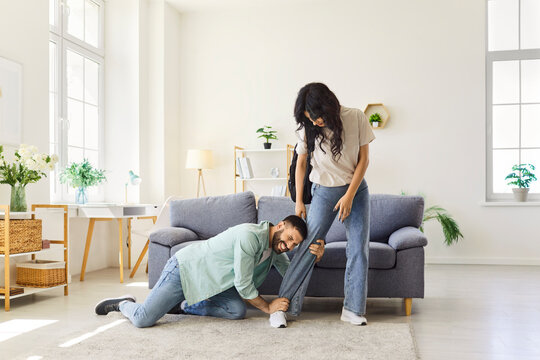 Couple quarrel, family problems and breakup at home, clingy man in despair and stress pleading with woman not to leave. Upset guy kneeling and clinging to partners leg, trying to stop girl leaving