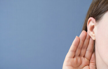 Woman listens attentively with her palm to her ear close-up on a blue background.