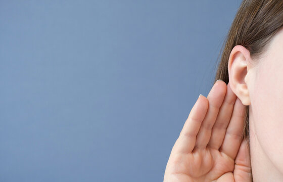 Woman listens attentively with her palm to her ear close-up on a blue background.