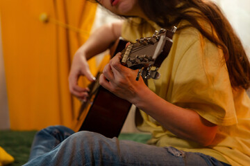 Close up of woman's hands plays guitar at home in her bedroom. She practices music skills on a bed. Creative hobby concept.