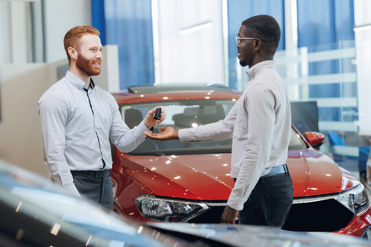 Agent seller in auto leasing giving key of car to man client after document contract signed in showroom