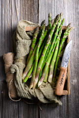 Fototapeta premium Fresh green asparagus bundle arranged with fabric napkin and knife on wooden background. Natural raw vegetables in food photography style. Flat lay, top view