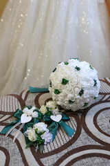 Wedding bouquet and boutonnieres of white roses with green ribbons against a sparkling dress background.