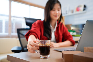 Architect sitting at desk in bright minimalist office, focusing on work with laptop and take coffee mug