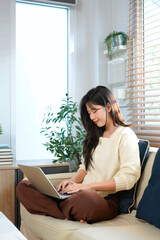 Obraz premium Laptop, young woman and working from home with a smile writing for website. Happy freelancer, living room sofa and female person blogging on a lounge couch and typing a blog post on a computer
