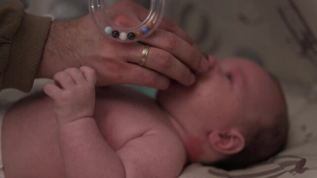 Father's gentle hand comforts newborn baby with a soft rattle toy in crib