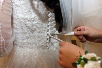 Hands tighten the corset of a lace sparkling wedding dress preparation before the ceremony.