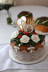 Festive wedding bread with white flowers and ring figures on a table in a celebration hall.