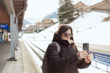 Fototapeta premium Young Woman Taking Photo with Smartphone at Train Station in Winter Switzerland 
