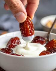 Close-up of a hand dipping a ripe Medjool date into a bowl of creamy white yogurt against a dark textured background with soft natural lighting