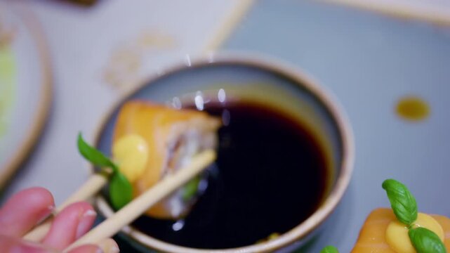 Close up pf chopsticks dipping a piece of sushi into soy sauce