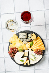 Cheese platter with craft cheese assortment on slate board at white tile background.