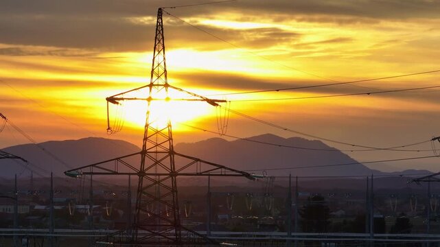 Crane of High-voltage electrical substation switchyard shows transformers and transmission lines during dramatic sunset sky in a rural area.