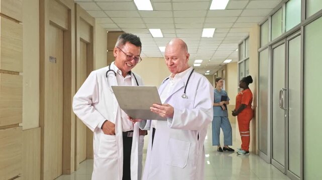Two doctors in white coats review a patient chart in a bright hospital corridor while medical staff in scrubs talk in the background