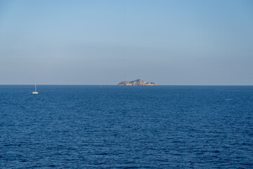 Sailboat on open sea with distant island in Tuscany, Italy