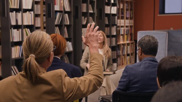 Back view slow motion shot of man with pony tail raising his hand to ask book author question during library presentation
