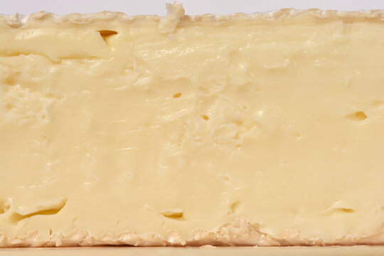 A macro close up showing the creamy interior of a brie cheese wedge with small holes and a soft pale yellow texture