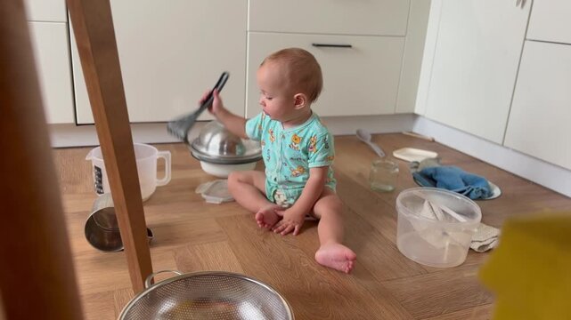 baby plays in the kitchen with pots and spoons. happy family kid dream concept. baby sits on the floor in the kitchen scattered pots kitchen utensils plays studies lifestyle