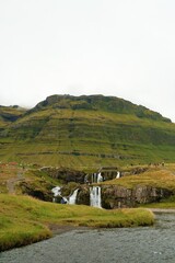 Scenic waterfall landscape in Iceland with green mountains and flowing river, popular travel destination.