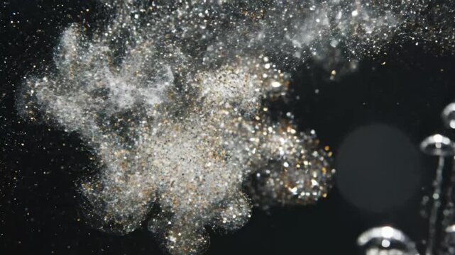 Water spray creates small droplets and patterns in dark background during slow motion capture near bright light source