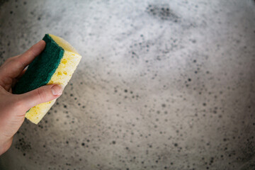 Hand holding sponge over soapy water