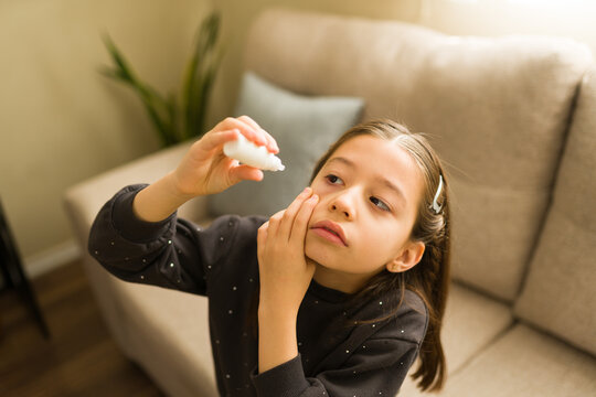 Little girl applying eye drops to her irritated red eye, treating a vision problem or allergy at home