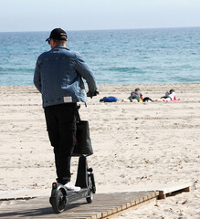 Patinete el&eacute;ctrico VMP scooter en playa y personas tumbadas junto al mar