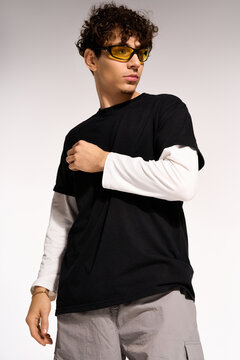 Stylish curly man in trendy outfit poses confidently in studio setting