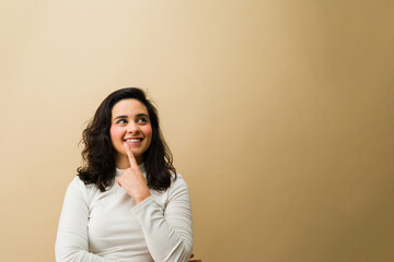 Cheerful woman thinking, looking up with a smiling, inspired expression, pointing finger to chin, having a new idea © AntonioDiaz