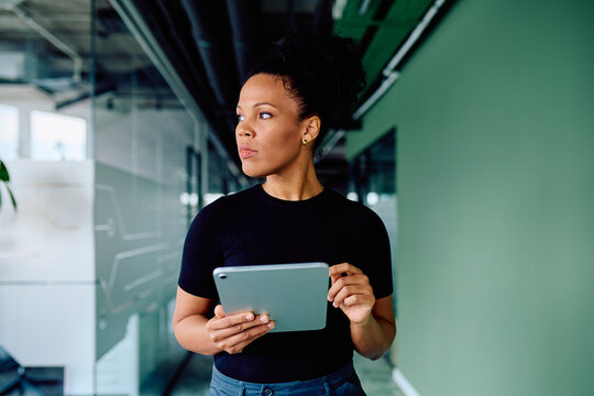 Confident businesswoman walking through a contemporary office space, holding a digital tablet and looking focused