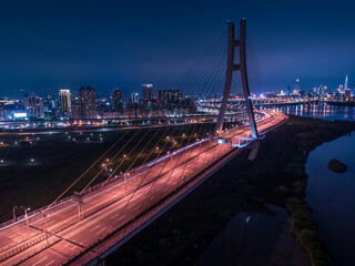 Fototapeta premium Car Light Trails of New Taipei Bridge - Long exposure of aerial photography use the drone at night in New Taipei, Taiwan.