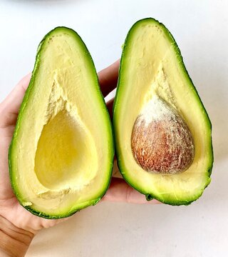 Fresh cut avocado halves held in hand with pit on white background