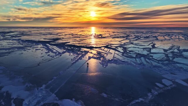 Vast frozen sea with people silhouettes walking on broken ice floes during a colorful sunset in arctic climate in Norway, aerial view