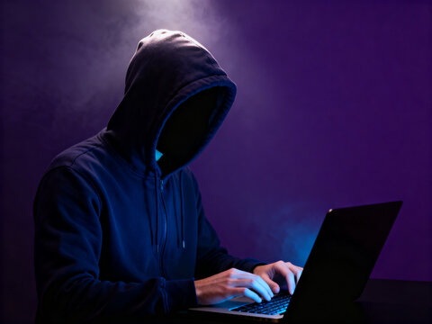 A masked criminal hacker stealing sensitive data from a business laptop using advanced cyber technology to commit information theft and fraud